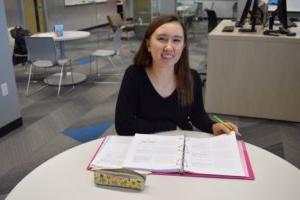 student sitting at table and smiling while turning a page in her binder