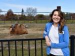 woman leaning against a railing with a camel in the background