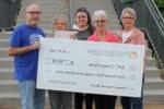 5 people standing outside Outreach Center with oversized check