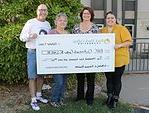 4 people standing outdoors holding oversized check